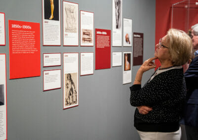 Exhibition attendee reading Bespoke Bodies exhibition panels with timeline of information from 1850s-1900s.
