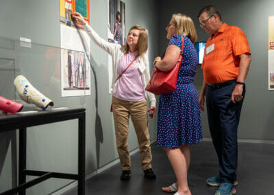 Three adults viewing Bespoke Bodies exhibition panels next to Alleles leg covers on display.