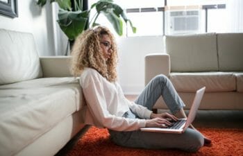 Woman sitting on floor in living room working on laptop