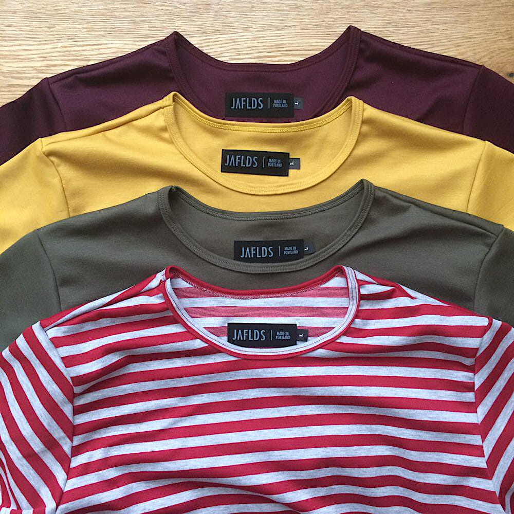 Four Jaefield basic t-shirts layered on top of each other. One is burgundy, another is yellow, the next is brown and the last shirt is red and white striped.