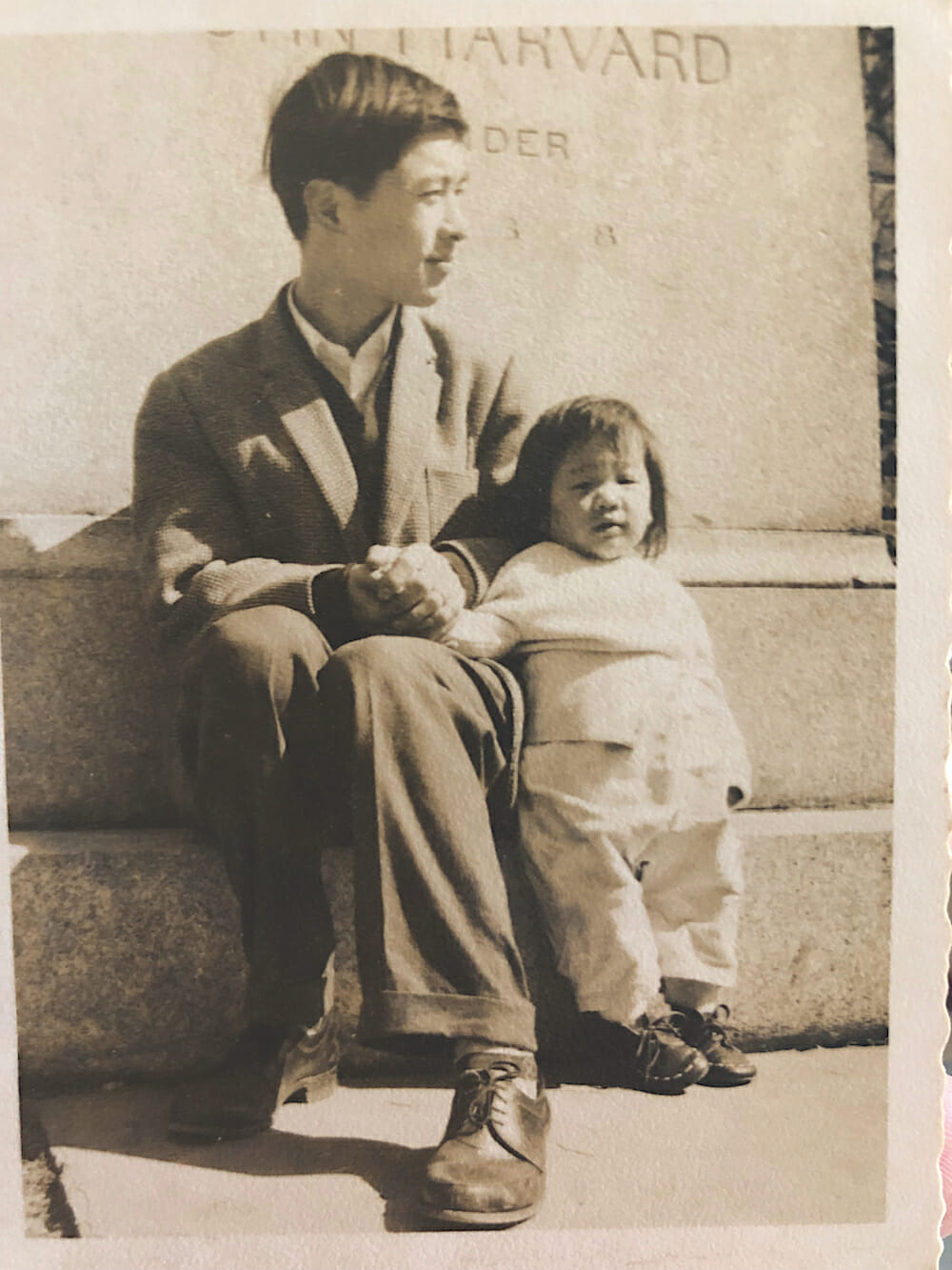 Suenn and her Father Picture of Suenn as a baby standing near her father who is seated at the base of a Harvard statue.