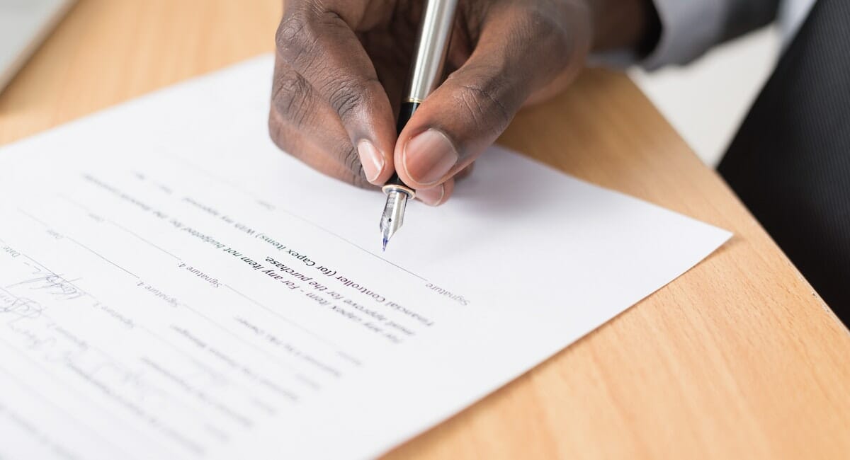 A close up of a hand signing a document with a fountain pen