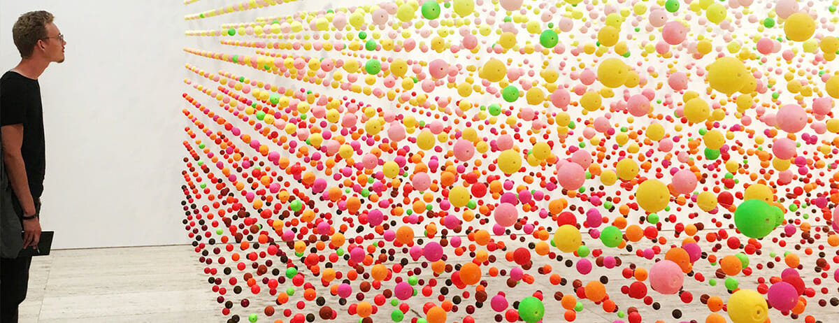 Person standing in front of sculptural wall of colored balls