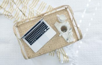 A photo of a laptop resting on a tray with coffee next to it on a bed