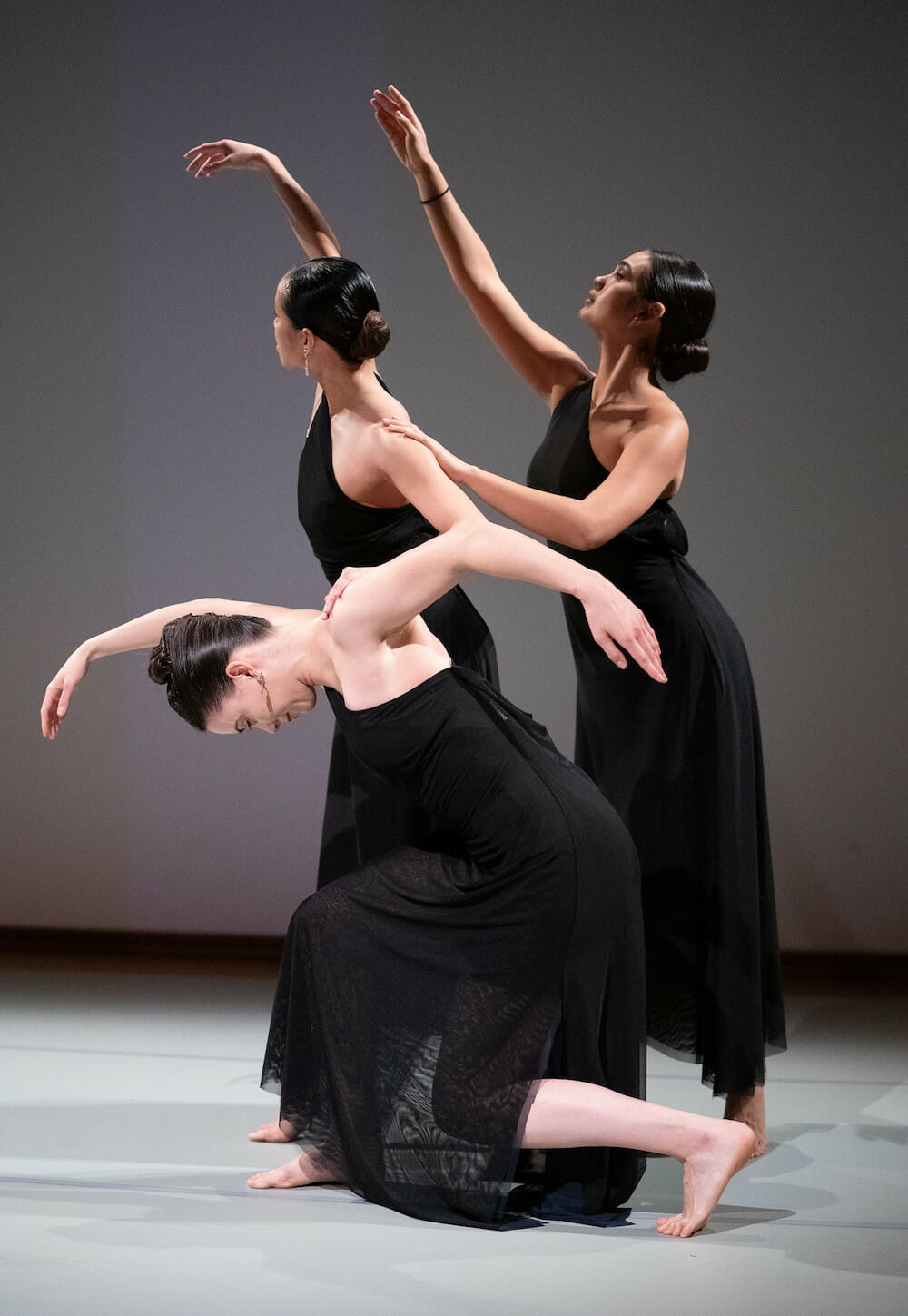 Three women in black dresses pose together with extended arms