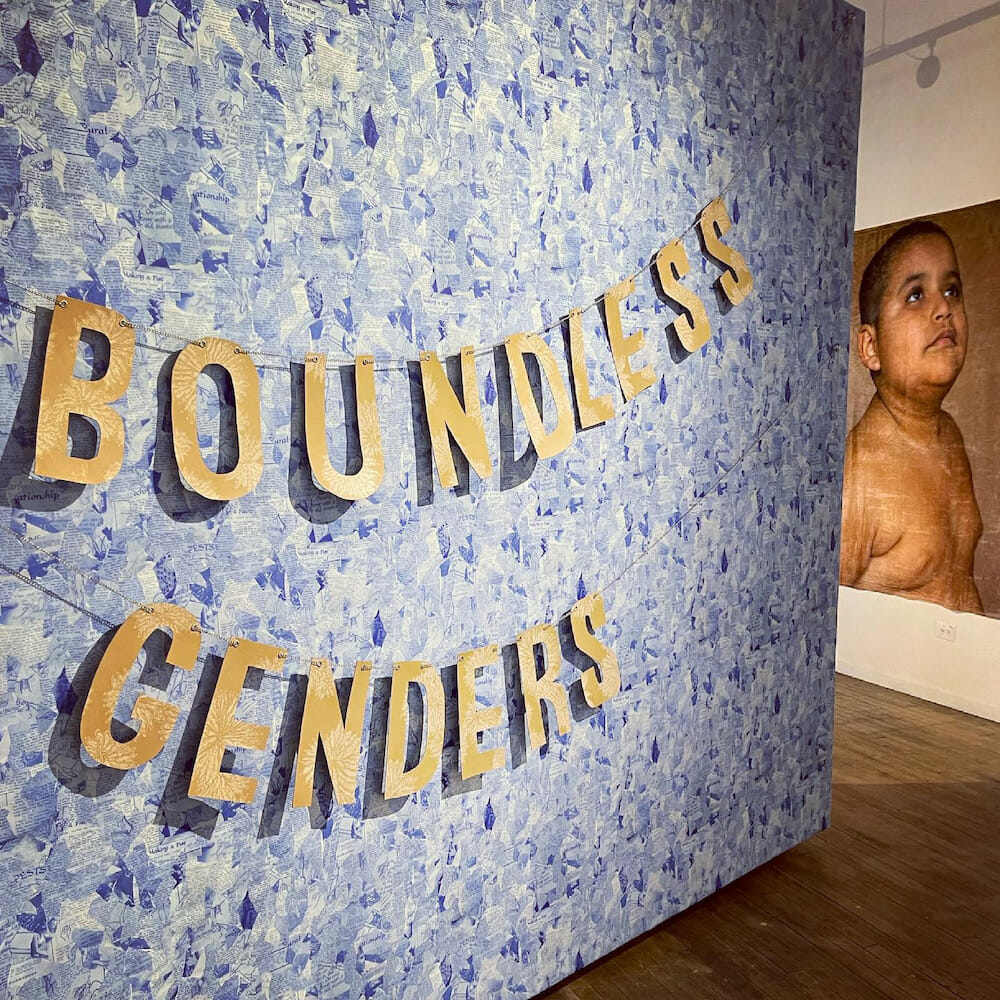 “Boundless genders” spelled out via a letter banner in front of a weathered portrait of a child, looking upward. 