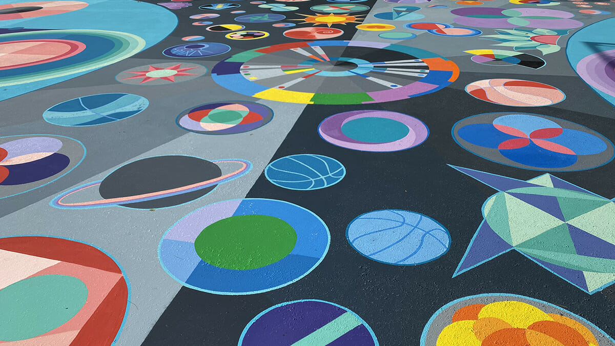 Basketball court painted with various abstract shapes by artist Maria Moteni.