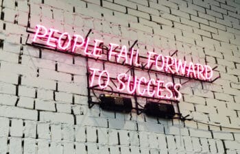 neon sign reading "People fail forward to success" on a white-washed interior brick wall